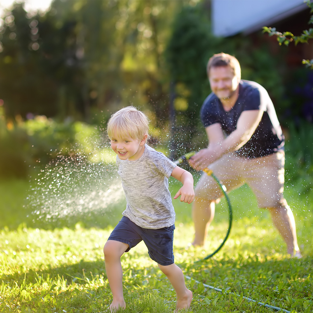 Mann mit Gartenschlauch und Kind